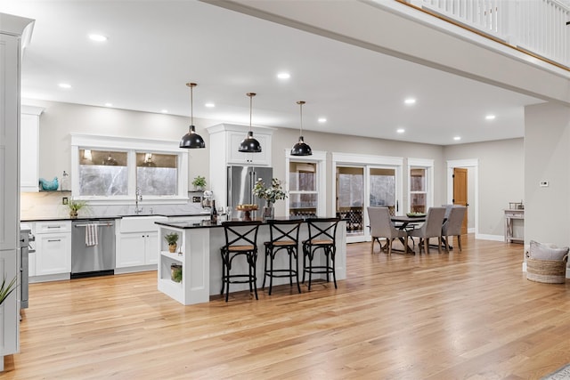 kitchen featuring white cabinets, appliances with stainless steel finishes, a kitchen island, decorative light fixtures, and a breakfast bar