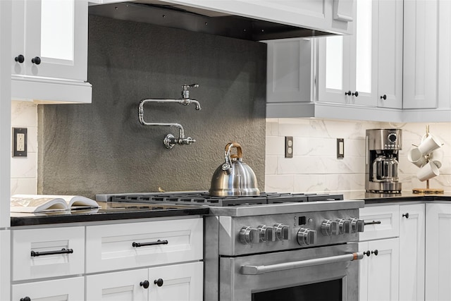 kitchen with white cabinets, high end stove, and tasteful backsplash