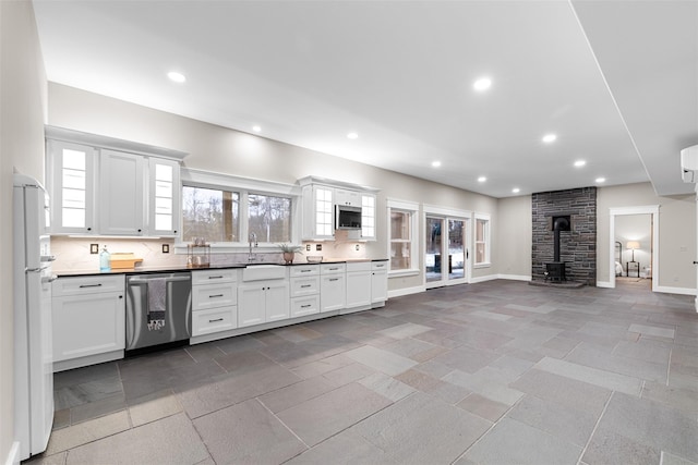 kitchen with white cabinetry, stainless steel appliances, a wood stove, backsplash, and sink