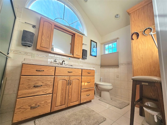 bathroom with toilet, vaulted ceiling, tile walls, vanity, and tile patterned flooring