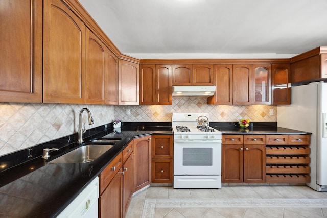 kitchen featuring tasteful backsplash, sink, white appliances, light tile patterned floors, and dark stone counters