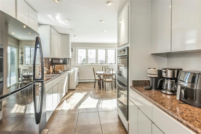 kitchen with dark stone countertops, black appliances, white cabinetry, light tile patterned floors, and a baseboard radiator