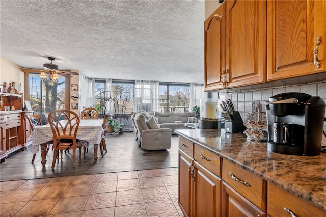 kitchen featuring a wall of windows, ceiling fan, tasteful backsplash, a textured ceiling, and dark stone counters