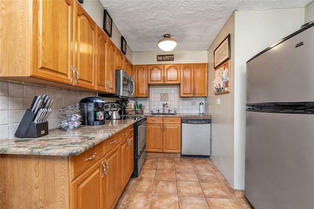 kitchen featuring stainless steel appliances, tasteful backsplash, light stone counters, a textured ceiling, and light tile patterned flooring