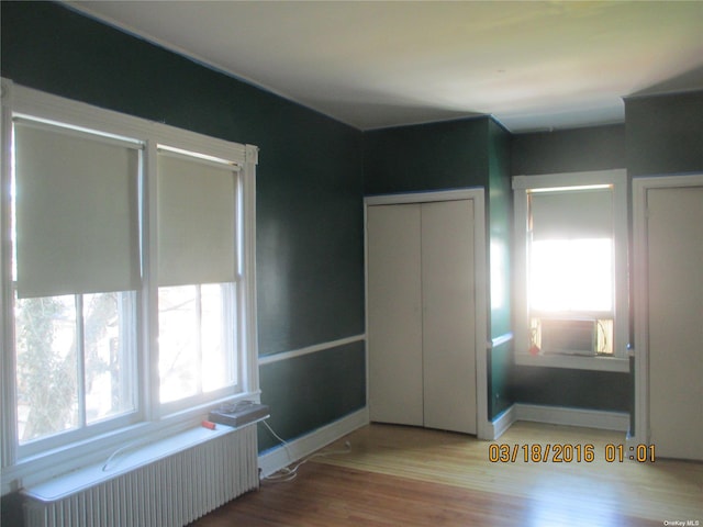 unfurnished bedroom featuring wood-type flooring, radiator heating unit, and cooling unit