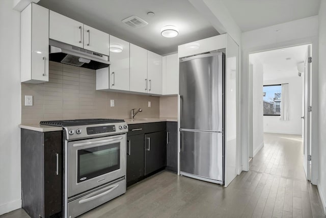 kitchen with wood-type flooring, appliances with stainless steel finishes, white cabinets, and decorative backsplash