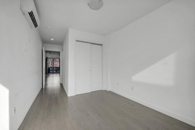 unfurnished bedroom featuring hardwood / wood-style flooring, a closet, and a wall mounted AC