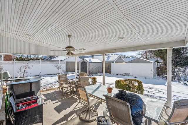 snow covered patio featuring ceiling fan and a shed