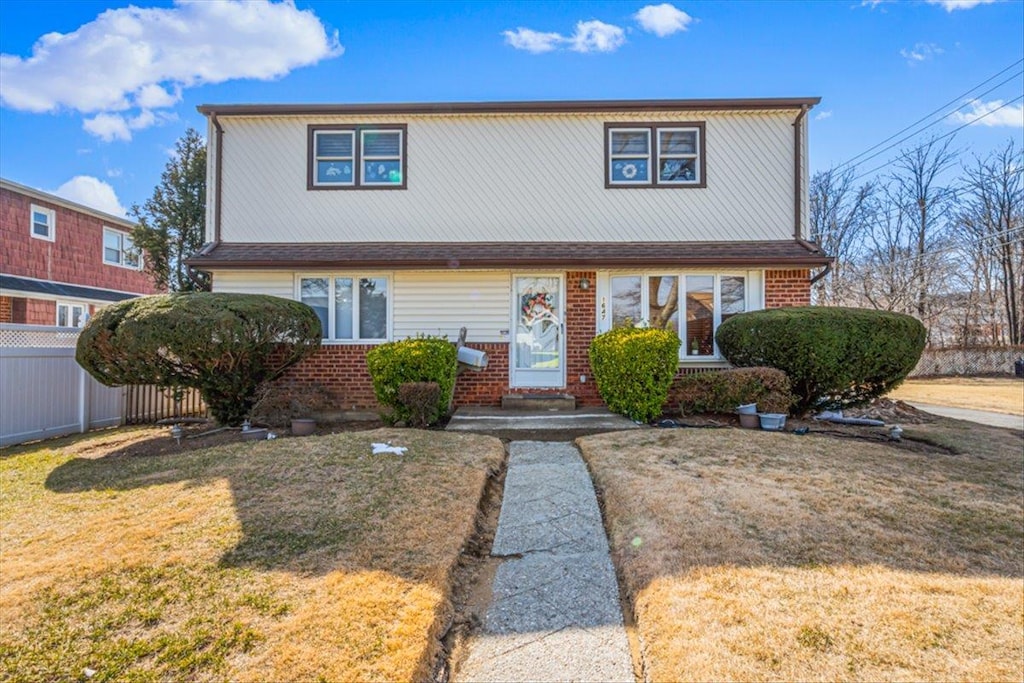 view of front of home with a front yard, brick siding, and fence