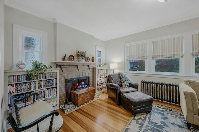 living area featuring radiator, a brick fireplace, crown molding, and hardwood / wood-style flooring