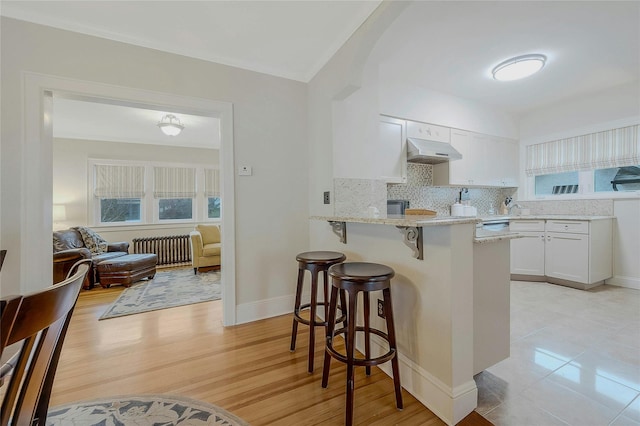 kitchen with white cabinets, radiator, a kitchen bar, light wood-type flooring, and light stone counters