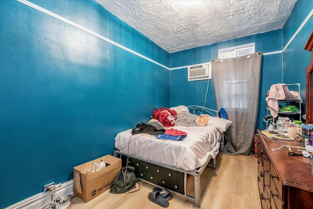 bedroom with light hardwood / wood-style floors, a textured ceiling, and a wall mounted air conditioner