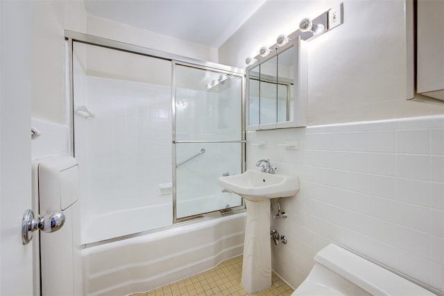 bathroom with enclosed tub / shower combo, toilet, tile patterned flooring, and tile walls