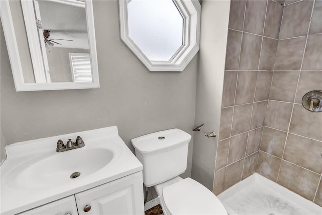 bathroom with ceiling fan, toilet, vanity, and tiled shower