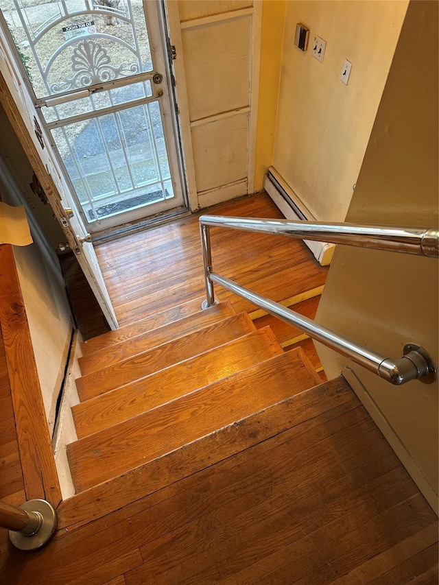 stairs with hardwood / wood-style floors and a baseboard heating unit