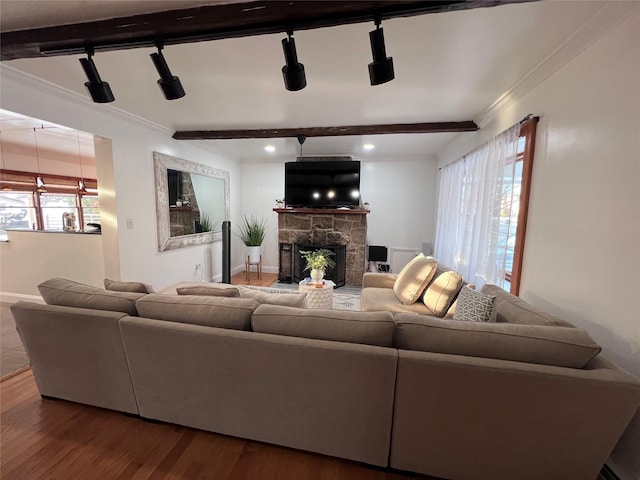 living room featuring rail lighting, a stone fireplace, wood-type flooring, and ornamental molding