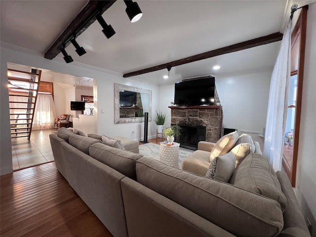 living room featuring beam ceiling, wood-type flooring, ornamental molding, track lighting, and a stone fireplace