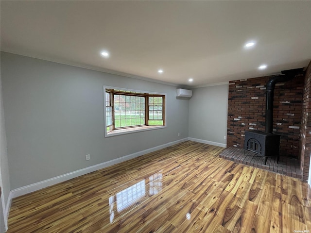 unfurnished living room with a wood stove, wood-type flooring, crown molding, and a wall unit AC