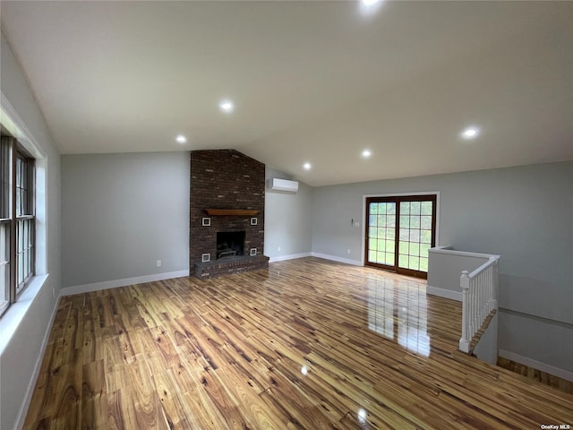 unfurnished living room featuring an AC wall unit, a brick fireplace, hardwood / wood-style flooring, and vaulted ceiling