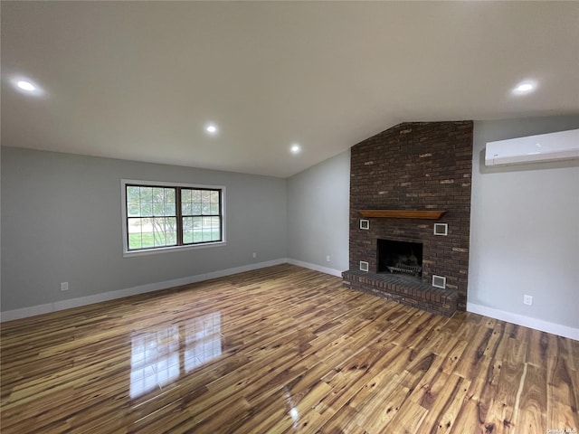 unfurnished living room featuring wood-type flooring, an AC wall unit, a brick fireplace, and vaulted ceiling