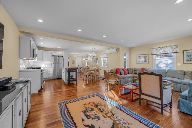 living room featuring hardwood / wood-style floors, a wall mounted air conditioner, and a notable chandelier