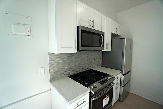 kitchen featuring light stone countertops, hardwood / wood-style floors, white cabinets, appliances with stainless steel finishes, and backsplash