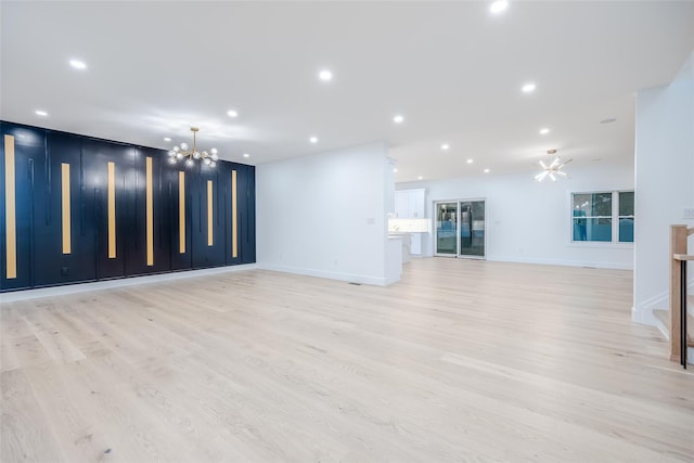 unfurnished living room with ceiling fan with notable chandelier and light hardwood / wood-style floors