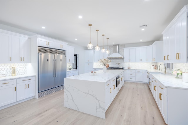 kitchen with backsplash, built in fridge, a kitchen island, wall chimney exhaust hood, and white cabinets