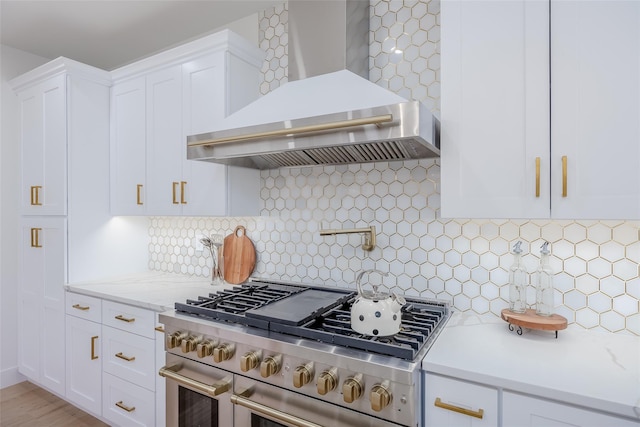 kitchen featuring light stone countertops, wall chimney exhaust hood, white cabinetry, range with two ovens, and decorative backsplash