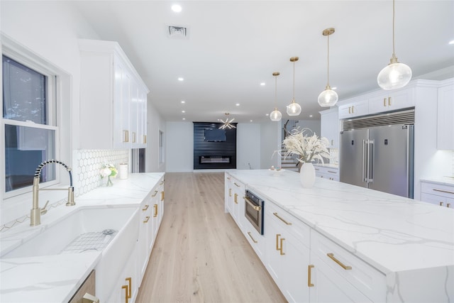 kitchen with decorative light fixtures, a fireplace, white cabinetry, stainless steel appliances, and light stone counters