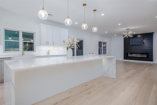 kitchen featuring backsplash, a spacious island, white cabinetry, hanging light fixtures, and light stone countertops