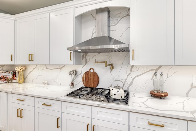 kitchen with stainless steel gas cooktop, decorative backsplash, white cabinets, and wall chimney range hood