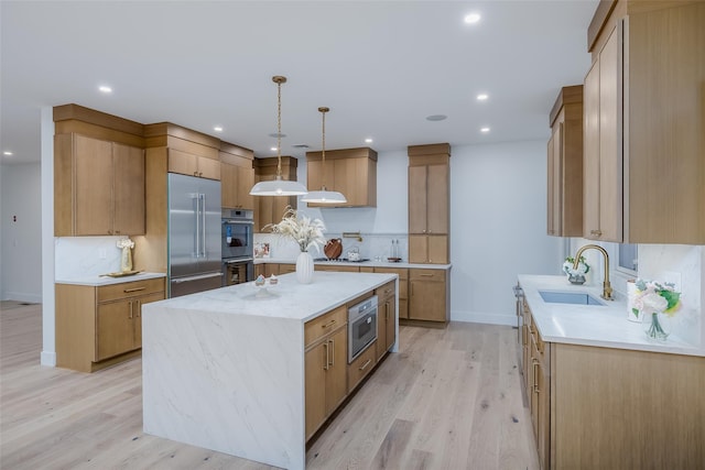 kitchen with appliances with stainless steel finishes, sink, light hardwood / wood-style floors, and a kitchen island