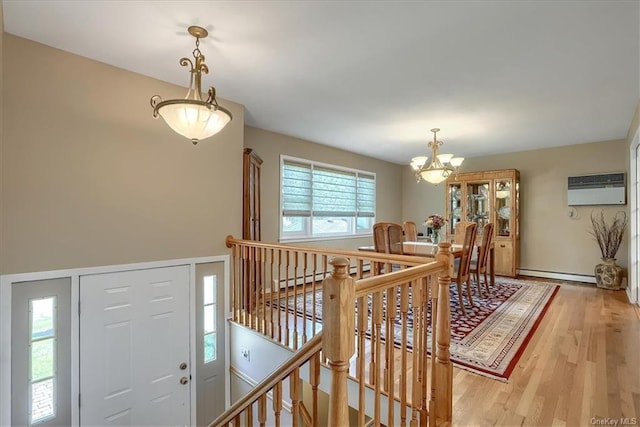 foyer with wood-type flooring, a healthy amount of sunlight, a wall mounted AC, and an inviting chandelier