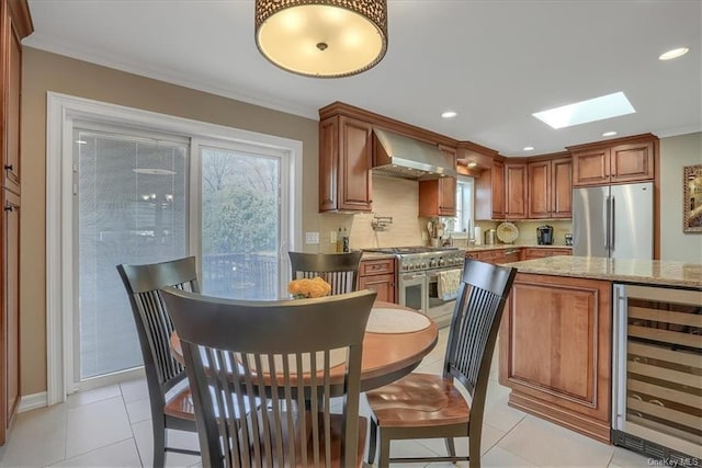 kitchen with light stone countertops, appliances with stainless steel finishes, wall chimney range hood, a skylight, and wine cooler