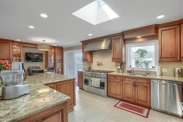 kitchen featuring pendant lighting, appliances with stainless steel finishes, sink, light stone countertops, and wall chimney range hood