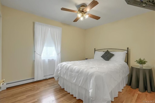 bedroom featuring ceiling fan, light hardwood / wood-style floors, and a baseboard heating unit