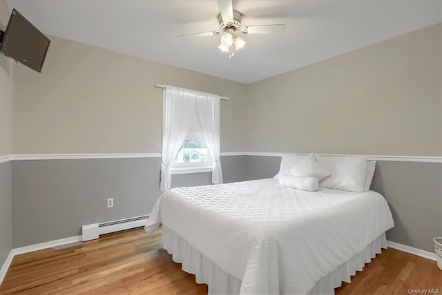 bedroom featuring ceiling fan, hardwood / wood-style flooring, and a baseboard heating unit