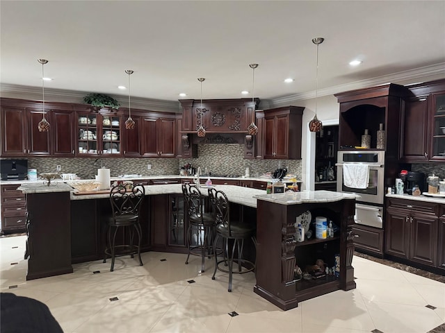 kitchen featuring decorative light fixtures, a kitchen breakfast bar, oven, and an island with sink