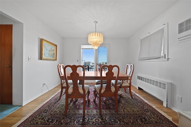 dining room featuring a wall mounted air conditioner, wood-type flooring, radiator, and an inviting chandelier