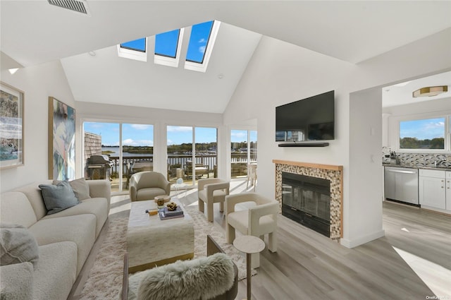 living room featuring a fireplace, light hardwood / wood-style flooring, high vaulted ceiling, and a skylight