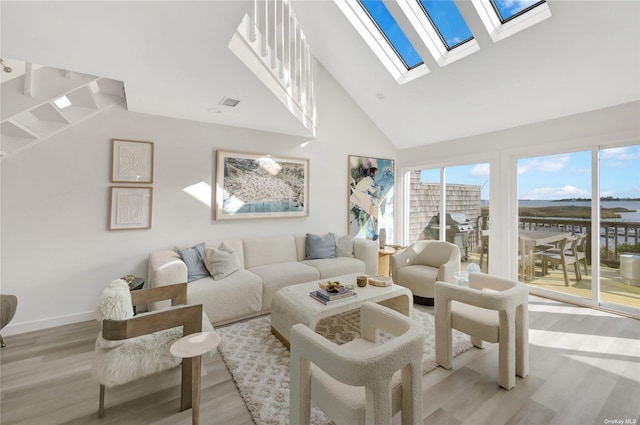 living room with light wood-type flooring, a skylight, and a high ceiling