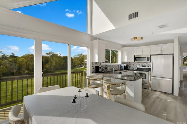 kitchen featuring light hardwood / wood-style flooring, white cabinets, dark stone countertops, decorative backsplash, and stainless steel appliances