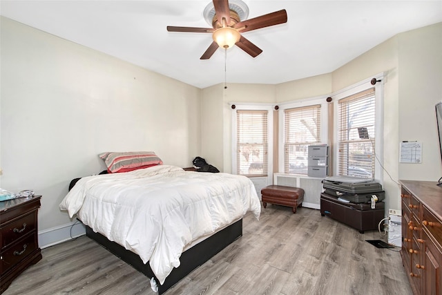 bedroom with a baseboard heating unit, radiator, ceiling fan, and light wood-type flooring