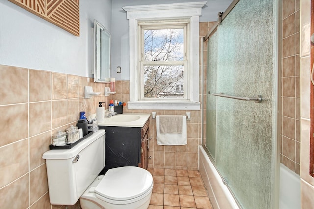 full bathroom featuring tile patterned floors, toilet, shower / bath combination with glass door, tile walls, and vanity