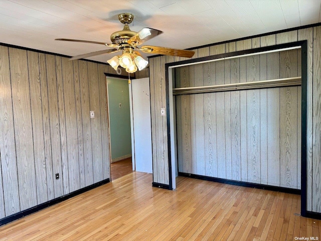 unfurnished bedroom featuring light wood-type flooring, a closet, wood walls, and ceiling fan