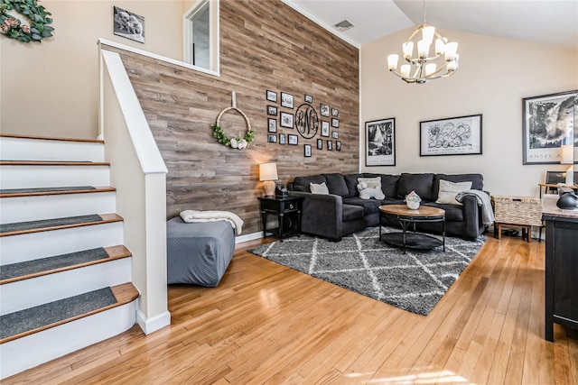 living area with visible vents, hardwood / wood-style flooring, wooden walls, an inviting chandelier, and stairs