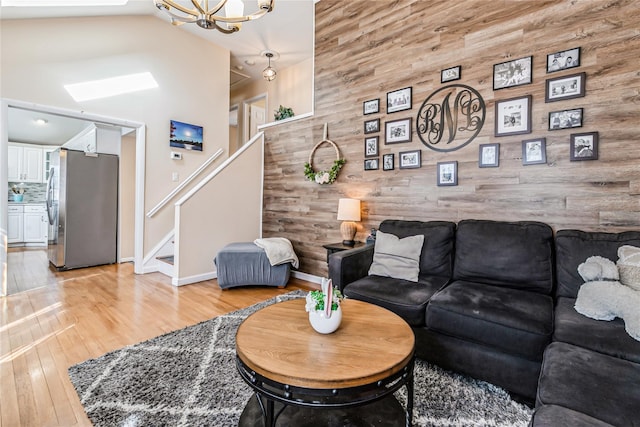 living area with a chandelier, light wood-style floors, wood walls, and stairs