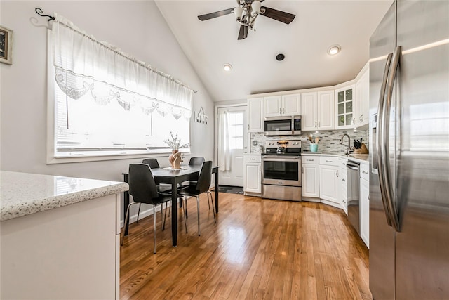 kitchen with ceiling fan, stainless steel appliances, vaulted ceiling, light wood-style floors, and tasteful backsplash