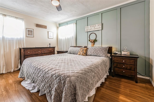 bedroom with a ceiling fan, a decorative wall, wood finished floors, and a textured ceiling